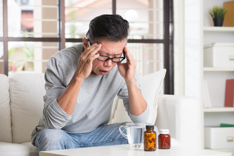 a middle-aged man with a headache leaning over tea and supplements